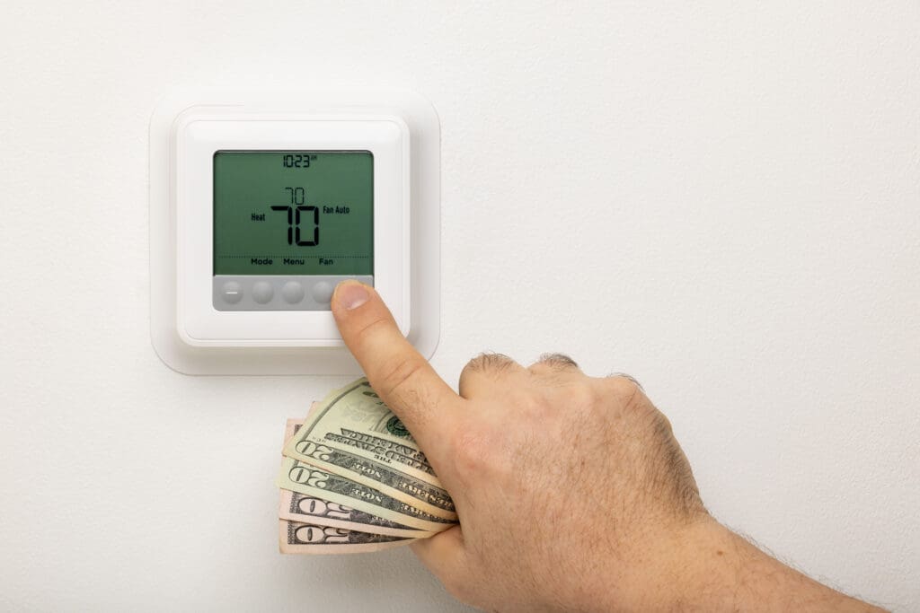Heating and Cooling Costs - A hand holding money adjusting a thermostat.